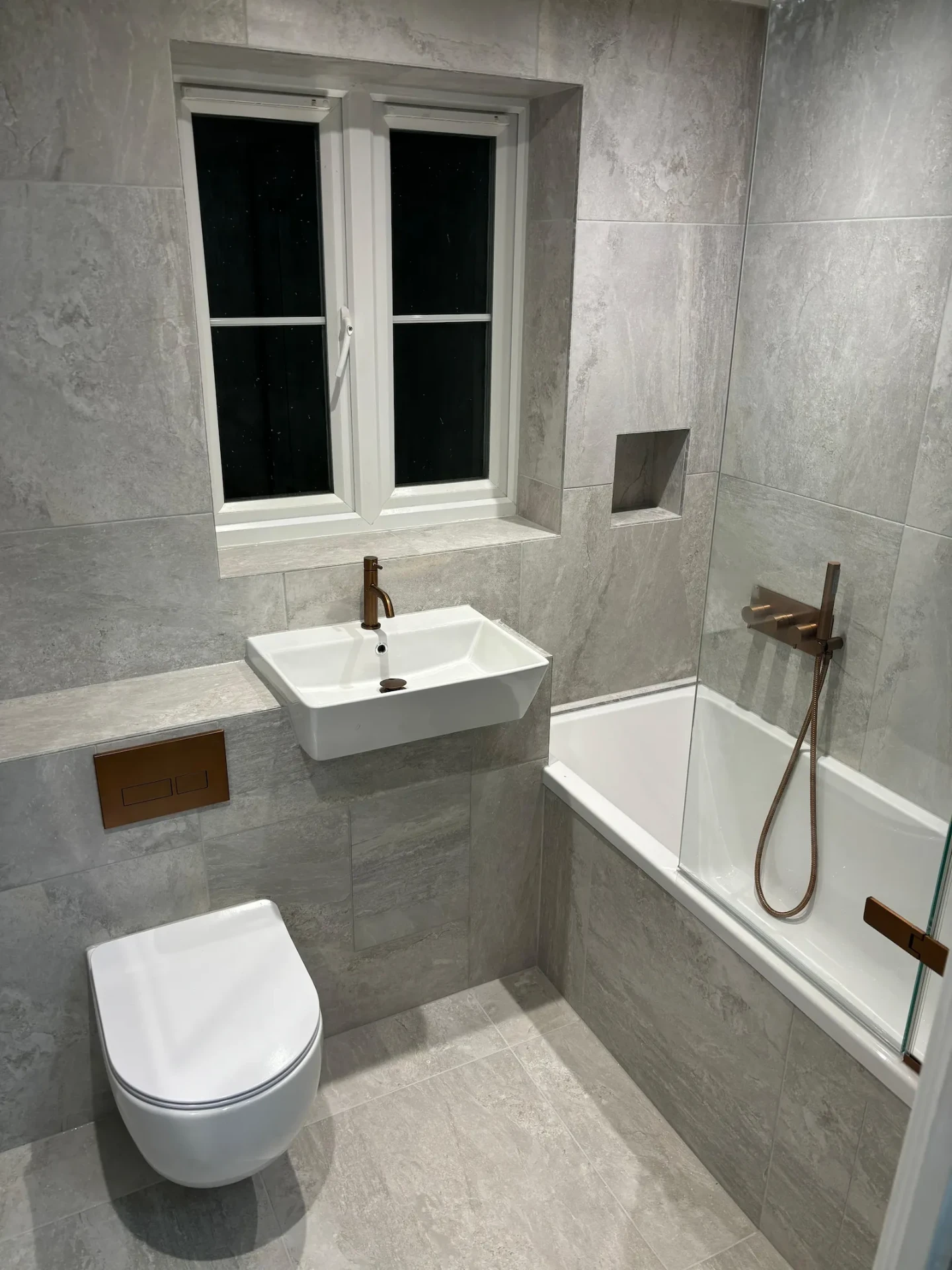 The same Emerson Park bathroom after renovation by Bridgerose, with stone tiling and copper-toned brassware