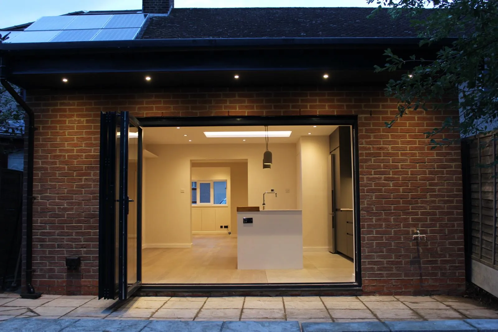 Brick rear extension at dusk with warm interior light through full-height glazing