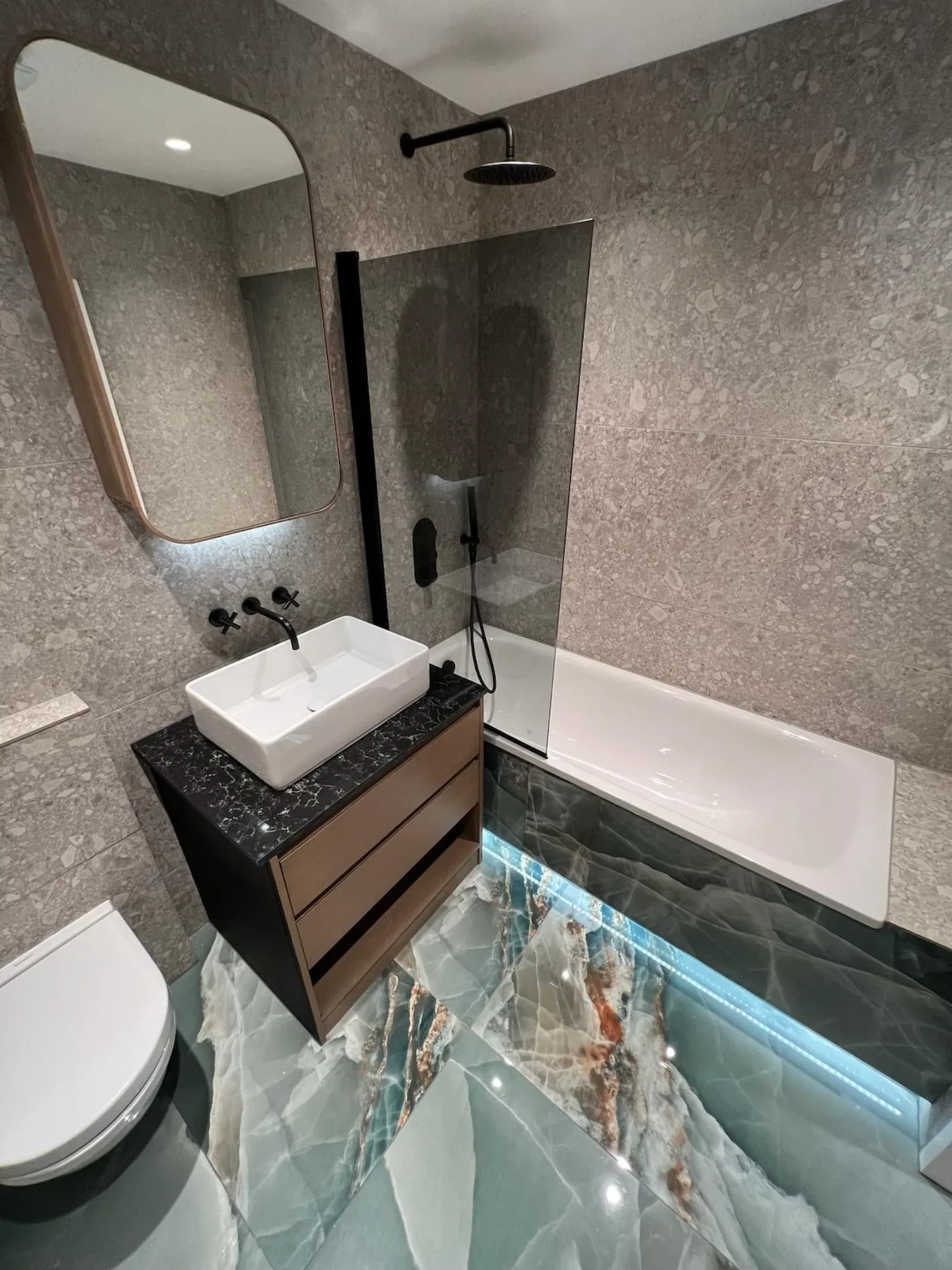 The same RM6 bathroom after full renovation by Bridgerose, with grey stone-effect tiling and a walk-in shower