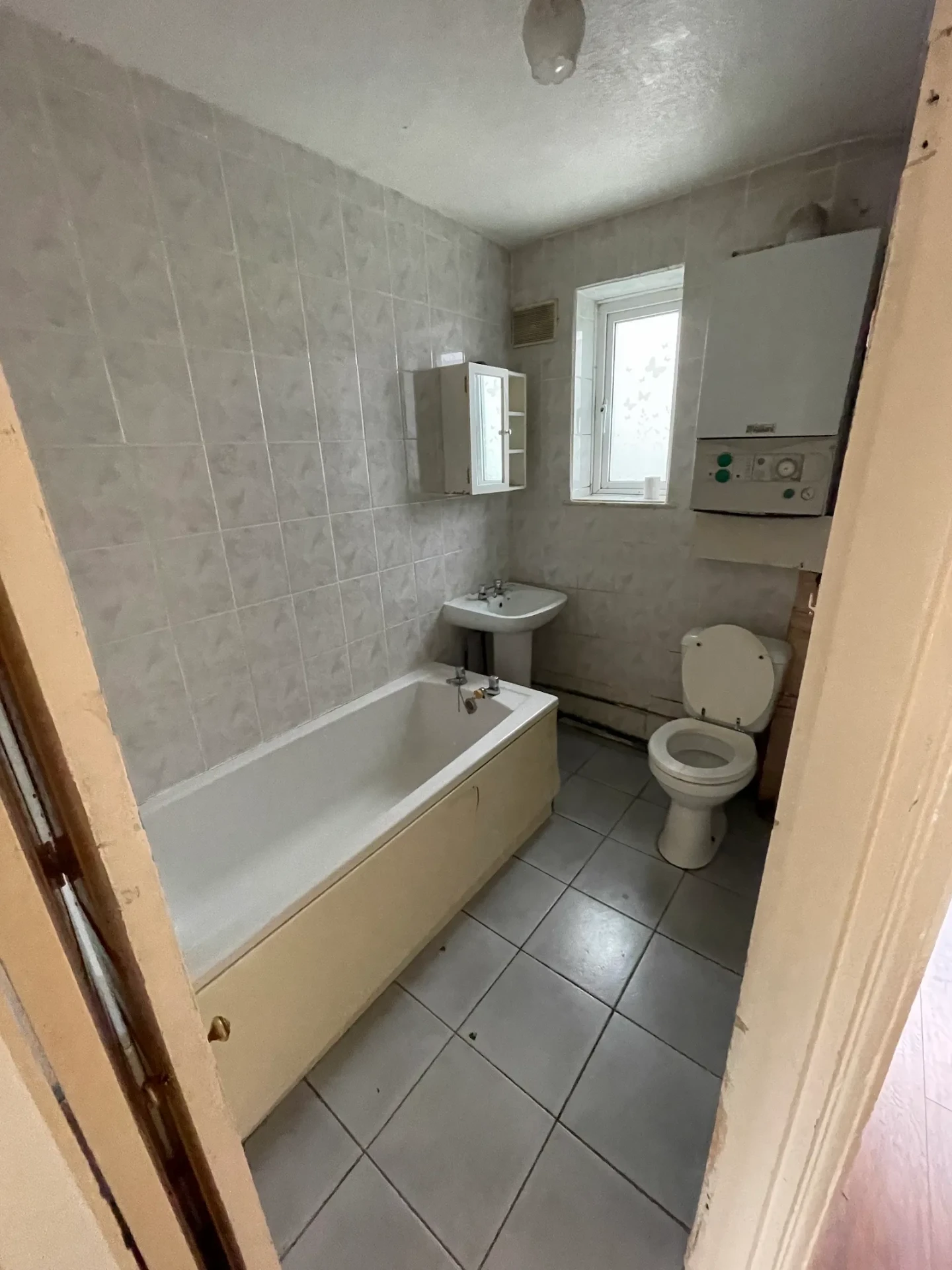 Dated bathroom in RM6 with beige wall tiles and an old panelled bath before renovation