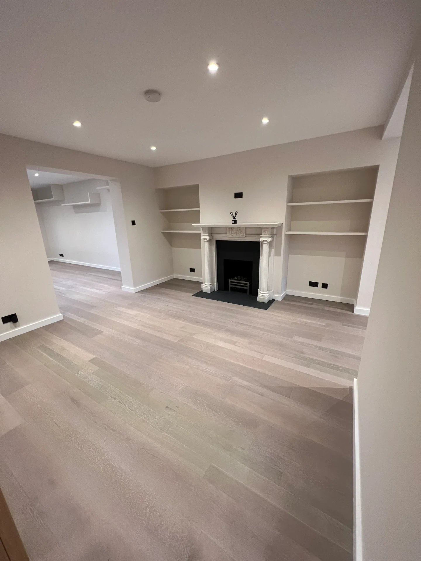 The same RM6 living room after renovation by Bridgerose, with light oak flooring and a white ornamental fireplace