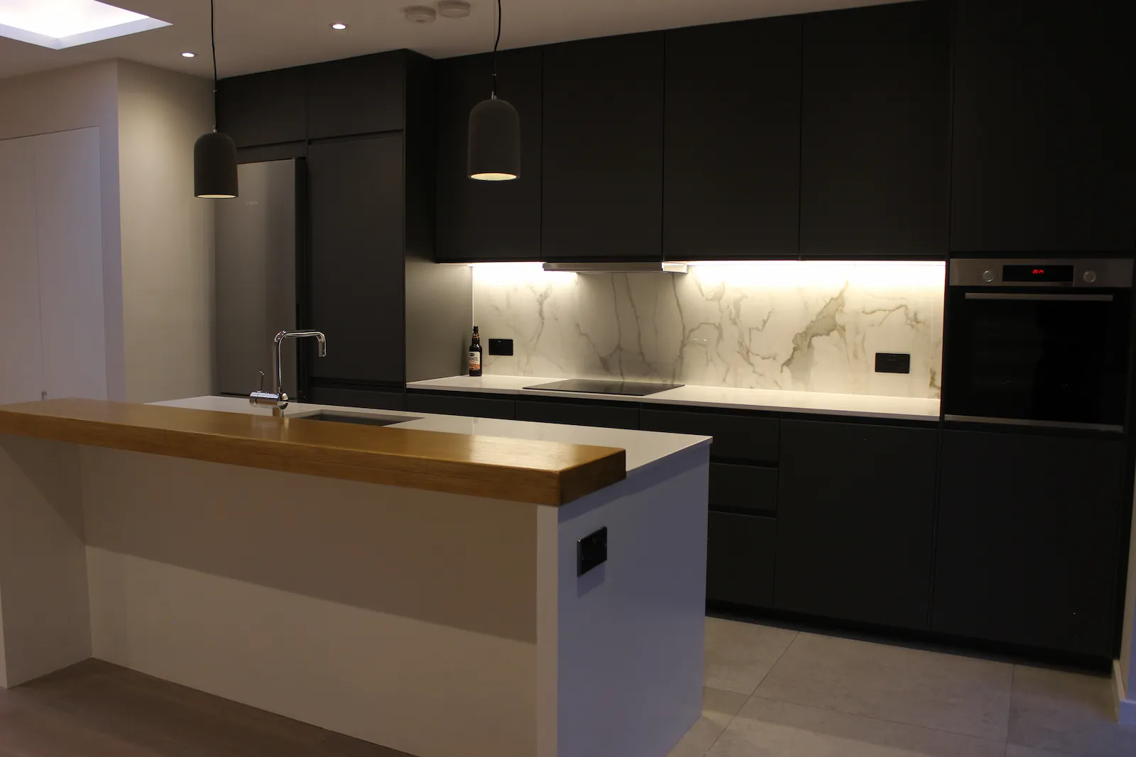 Dark handleless kitchen units with marble backsplash and pendant lighting in the RM6 house