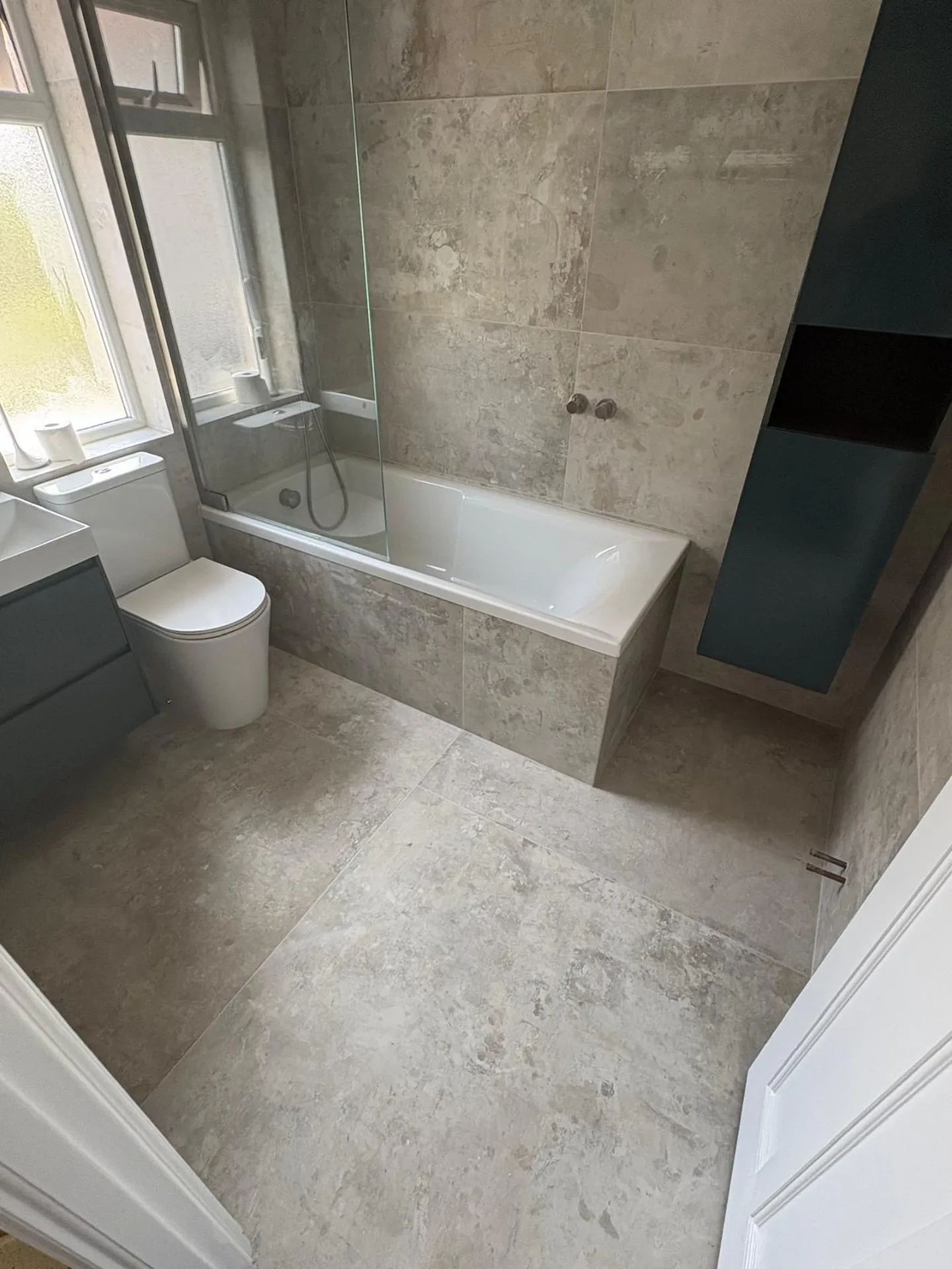 The same Upminster bathroom after renovation by Bridgerose, with grey textured tiling and a dark timber vanity unit